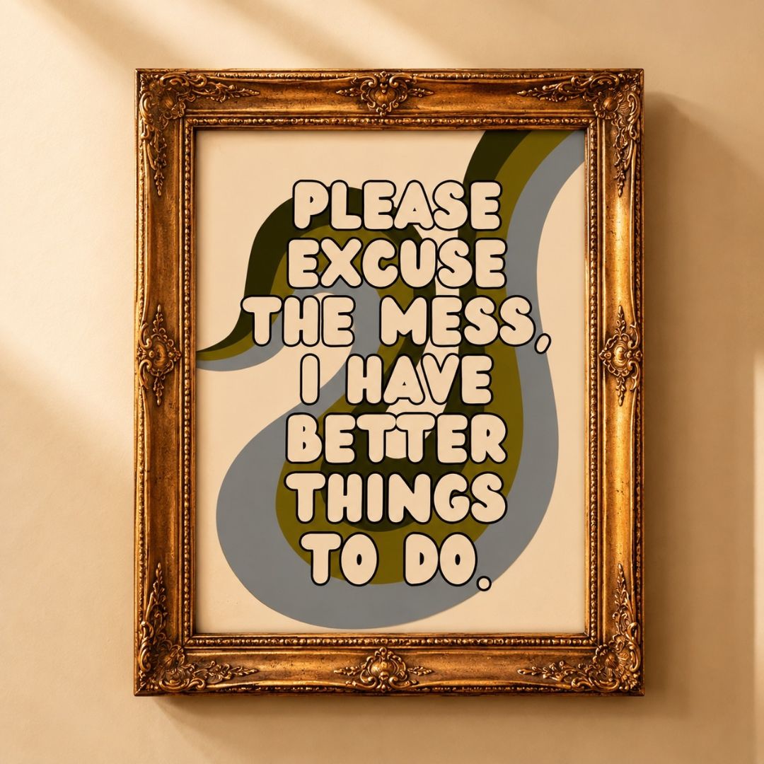 A framed typographic wall art print hangs on a beige wall. The artwork features a large gray-blue and olive green abstract shape with cream text reading, 'PLEASE EXCUSE THE MESS, I HAVE BETTER THINGS TO DO.