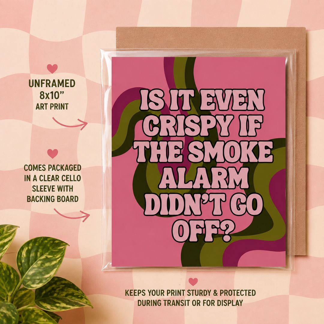 A square art print with a pink and green retro wavy background and bold text reading “IS IT EVEN CRISPIFY IF THE SMOKE ALARM DIDN’T GO OFF?” shown in a clear sleeve with kraft backing, on a pink plaid backdrop with decorative text callouts and a plant leaf.