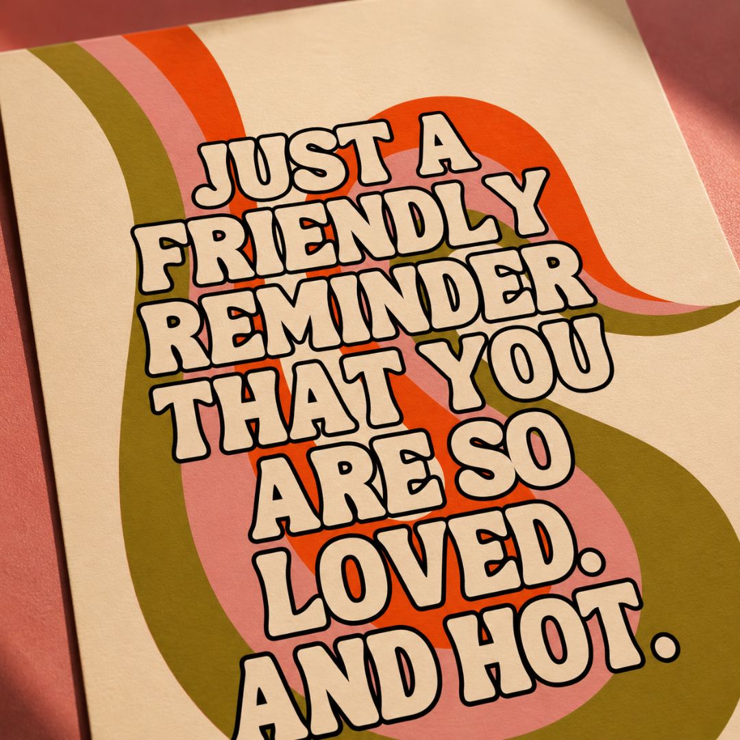 A close-up of a retro-style printed card or poster with bold cream text reading “JUST A FRIENDLY REMINDER THAT YOU ARE SO LOVED. AND HOT.