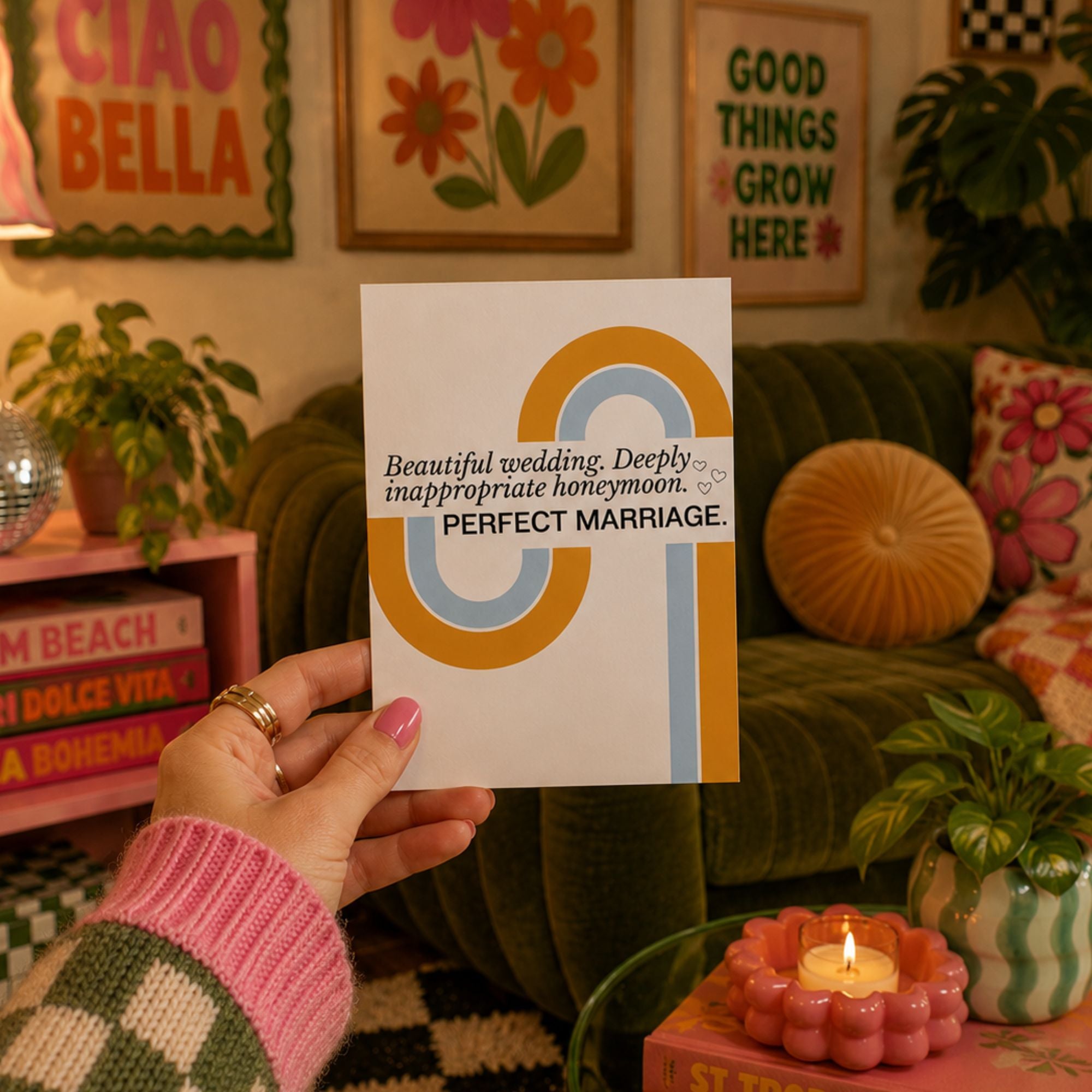 A hand holds a white wedding card featuring a retro-style yellow and blue circular design and the text 'Beautiful wedding. Deeply inappropriate honeymoon.