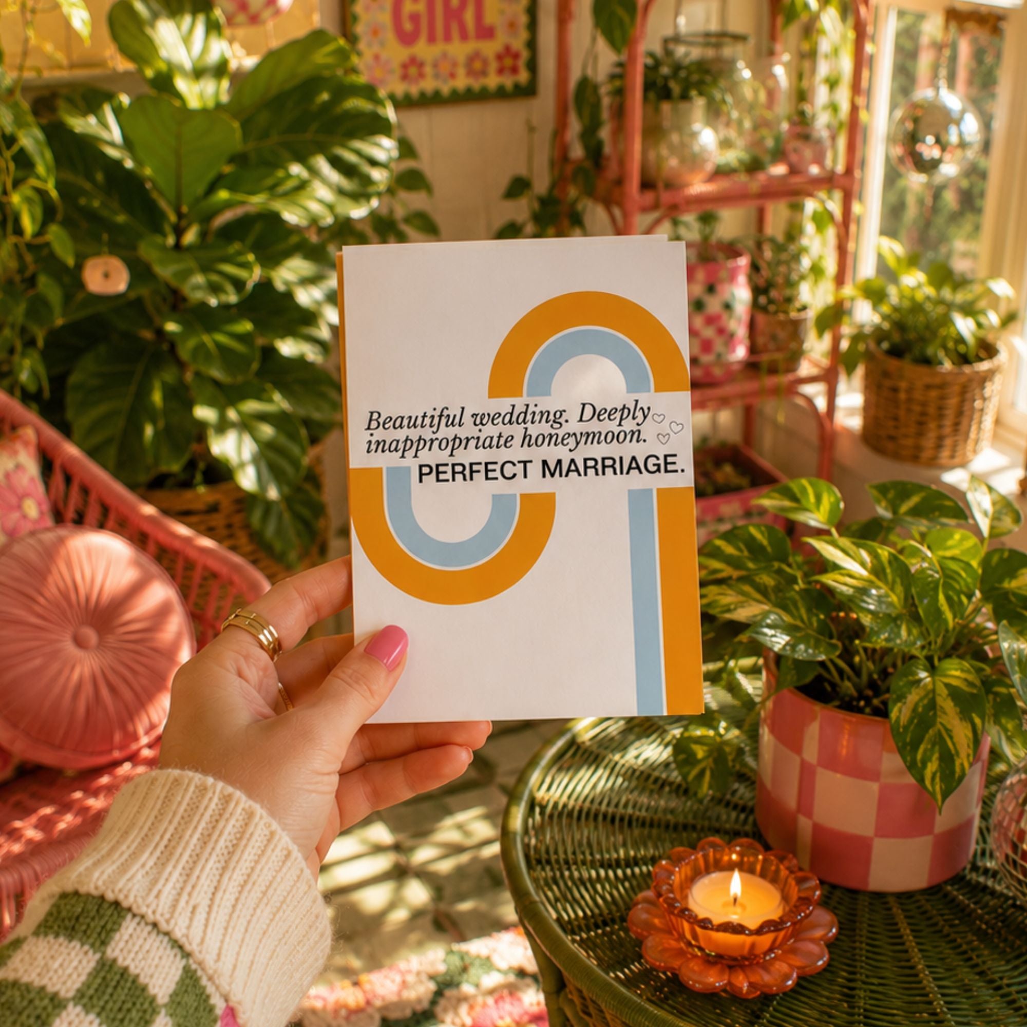 A hand holds a white greeting card with a colorful abstract design and the text 'Beautiful wedding. Deeply inappropriate honeymoon.