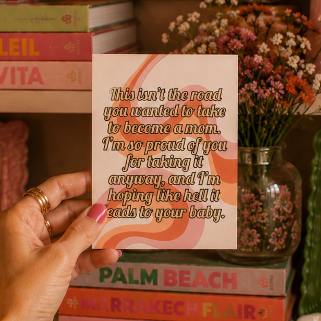 A hand holds a square greeting card with a humorous quote for a mom. The card has a cream background with retro wavy orange and pink stripes and brown text.